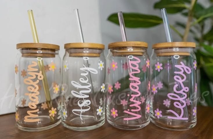 Four glass jars with names and floral designs on a wooden surface.
