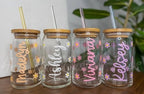 Four glass jars with names and floral designs on a wooden surface.