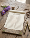 To-do list notepad on a wooden surface with flowers and pens.