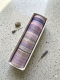 Set of washi tape rolls in a box on a textured surface with lavender flowers.