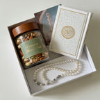 Gift set with a jar of mixed nuts, a Quran, and a pearl necklace on a white background