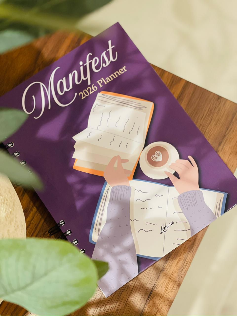 Levara Manifest 2026 productivity planner with purple cover featuring an illustration of hands writing and drinking coffee
