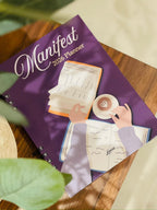 Levara Manifest 2026 productivity planner with purple cover featuring an illustration of hands writing and drinking coffee